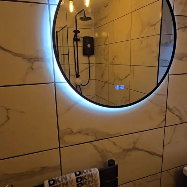 LED-backlit round mirror on marble-effect wall tiles with black shower fixtures