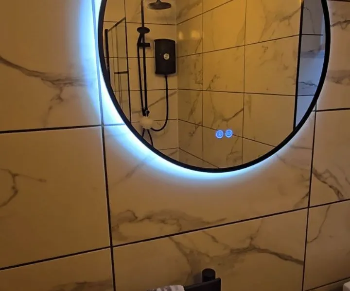 LED-backlit round mirror on marble-effect bathroom wall tiles