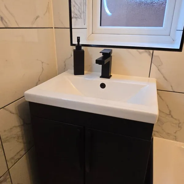 Wall-mounted black vanity unit with matte black tap and marble wall tiles