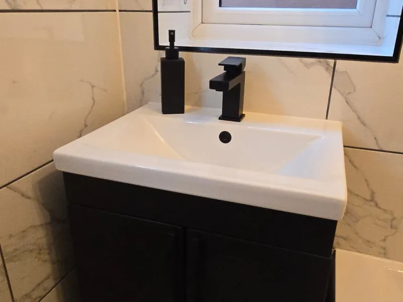 Wall-mounted black vanity unit with matte black tap and marble tiles