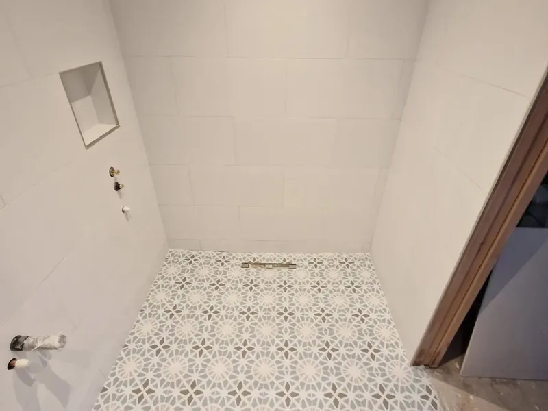 Walk-in shower with geometric patterned floor tiles and white wall tiles with recessed niche
