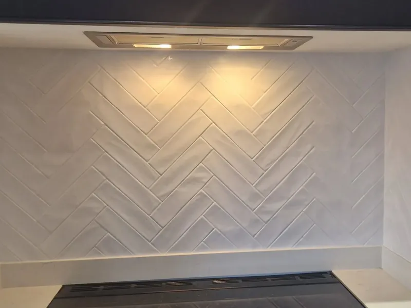 White herringbone tile backsplash installed behind a kitchen cooktop