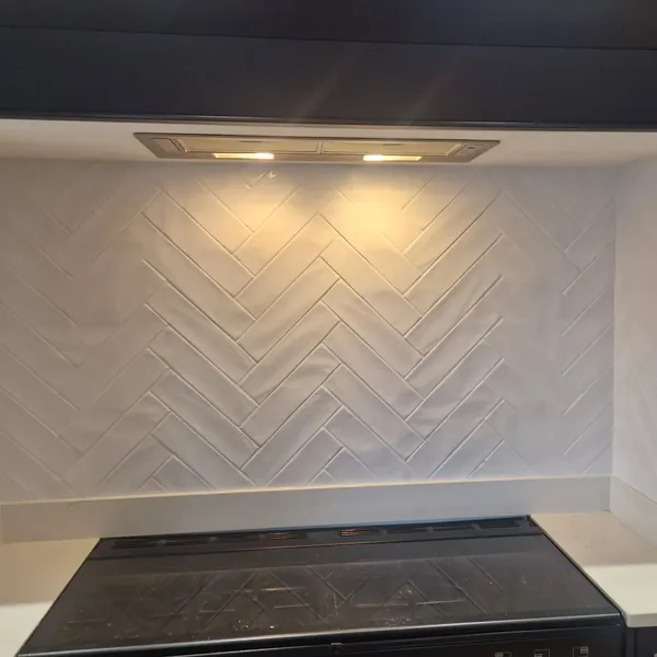 White herringbone tile backsplash behind kitchen cooktop
